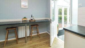 A kitchen with a dark countertop, wooden stools, and a view through an open door to a balcony. - Croyde Pebbles (Braunton)