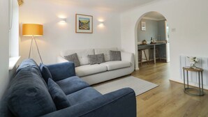 A modern living room with a blue sofa, a white sofa with patterned cushions, a floor lamp, and a painting on the wall. - Croyde Pebbles (Braunton)