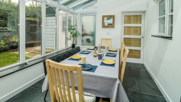 A conservatory with a dining table set for four, surrounded by chairs, with a view of the garden outside. - Croyde Pebbles (Braunton)