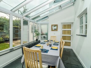 A conservatory with a dining table set for four, surrounded by chairs, with a view of the garden outside. - Croyde Pebbles (Braunton)