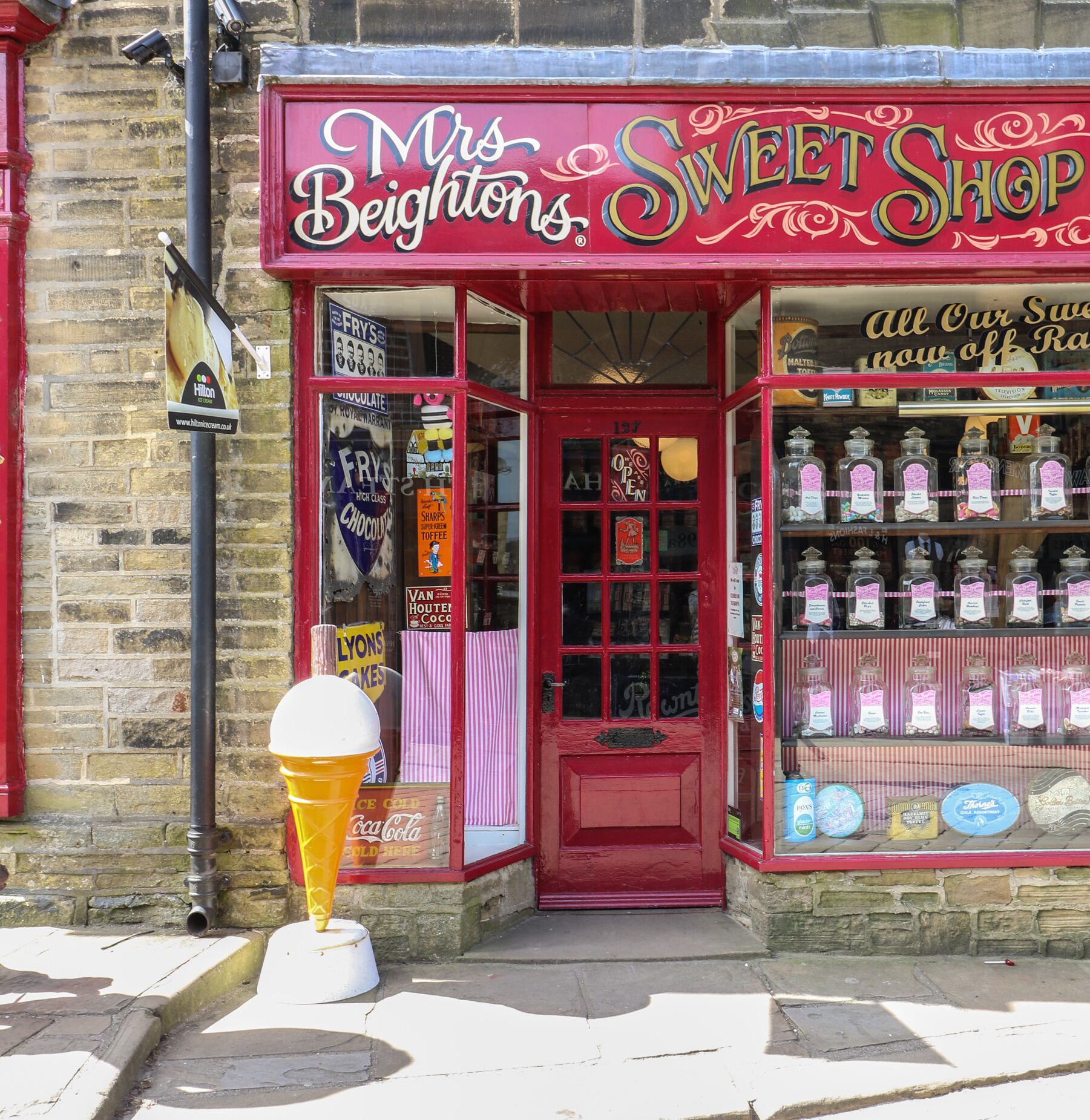 A storefront with a red awning and a sign reading "Mrs. Beighton’s Sweet Shop".