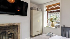 A bedroom with a fireplace, a wardrobe, a bed, and a window with a view. - The Snug on the Cobbles (Keighley)