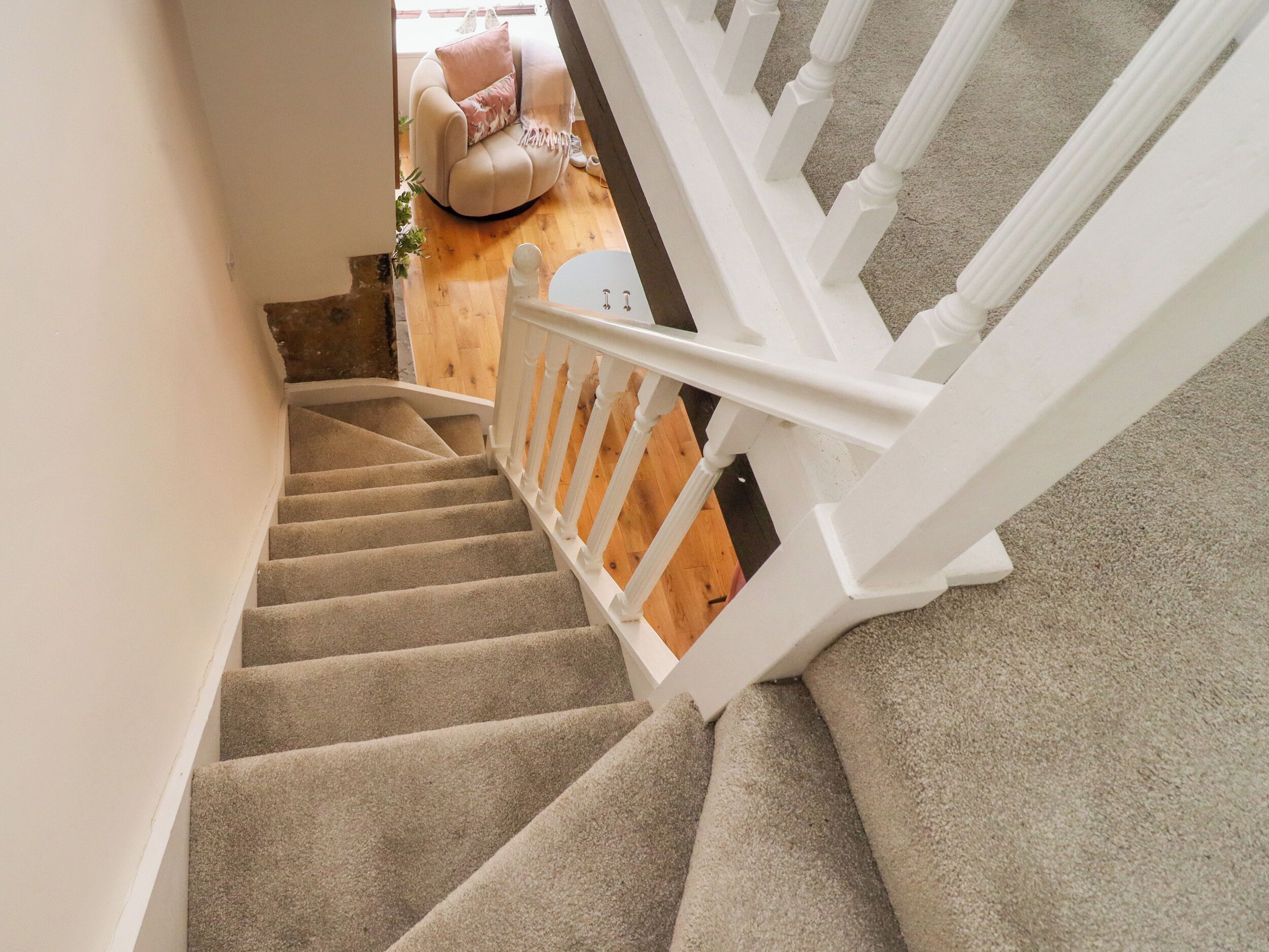 A carpeted staircase with white balusters, leading to a room with a wooden floor and a large window.