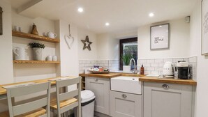 A modern kitchen with a wooden dining table, white cabinets, and a built-in sink. - The Snug on the Cobbles (Keighley)