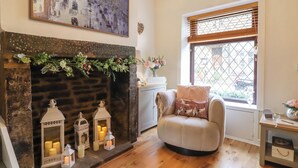 A cozy living room with a fireplace, a comfortable armchair, and a window with blinds. - The Snug on the Cobbles (Keighley)