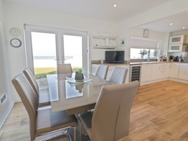 A modern kitchen with a dining area, large windows, and a view of the sea.