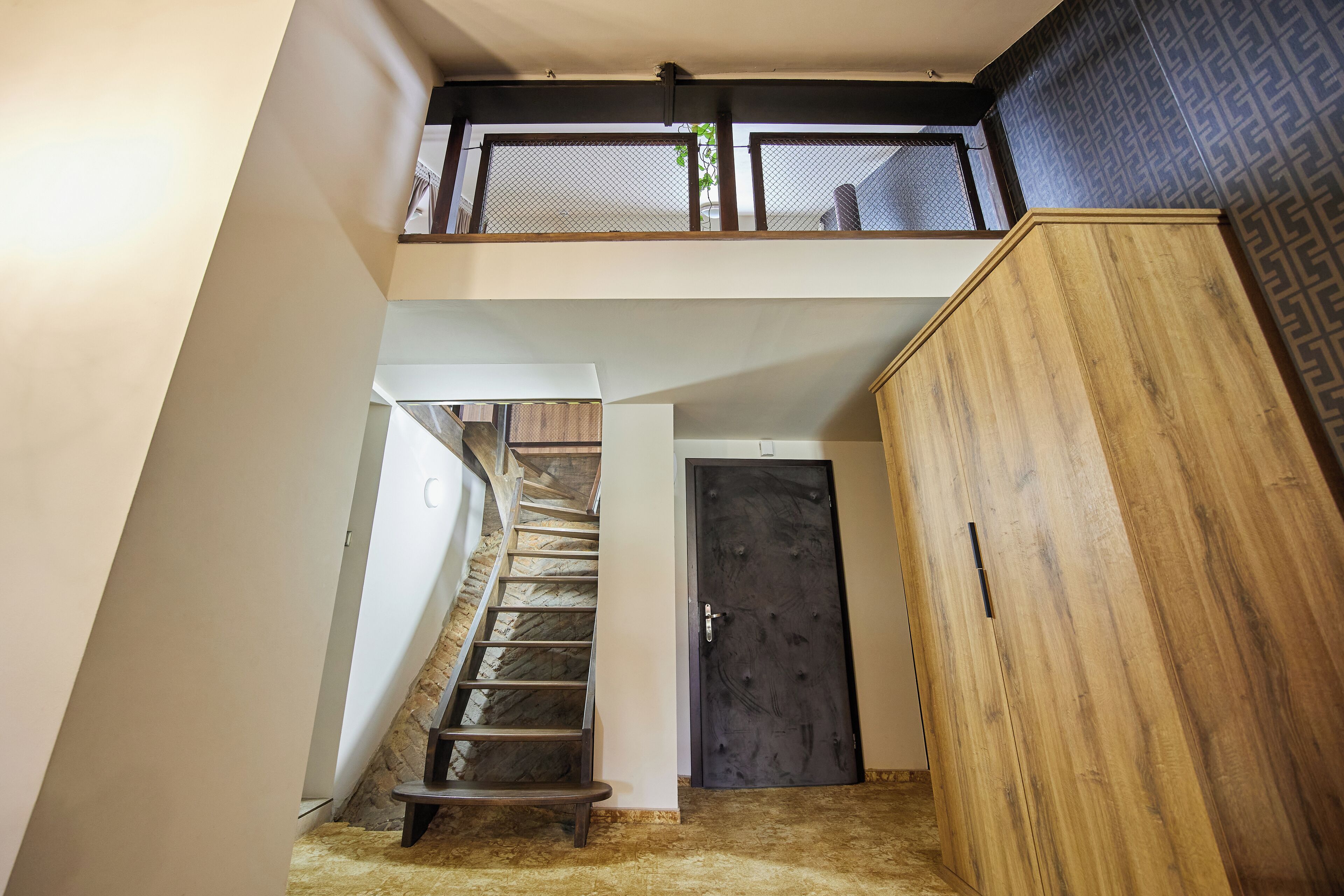 A staircase leading to a loft area with a mesh railing, a dark wooden door, and a large wooden cabinet.