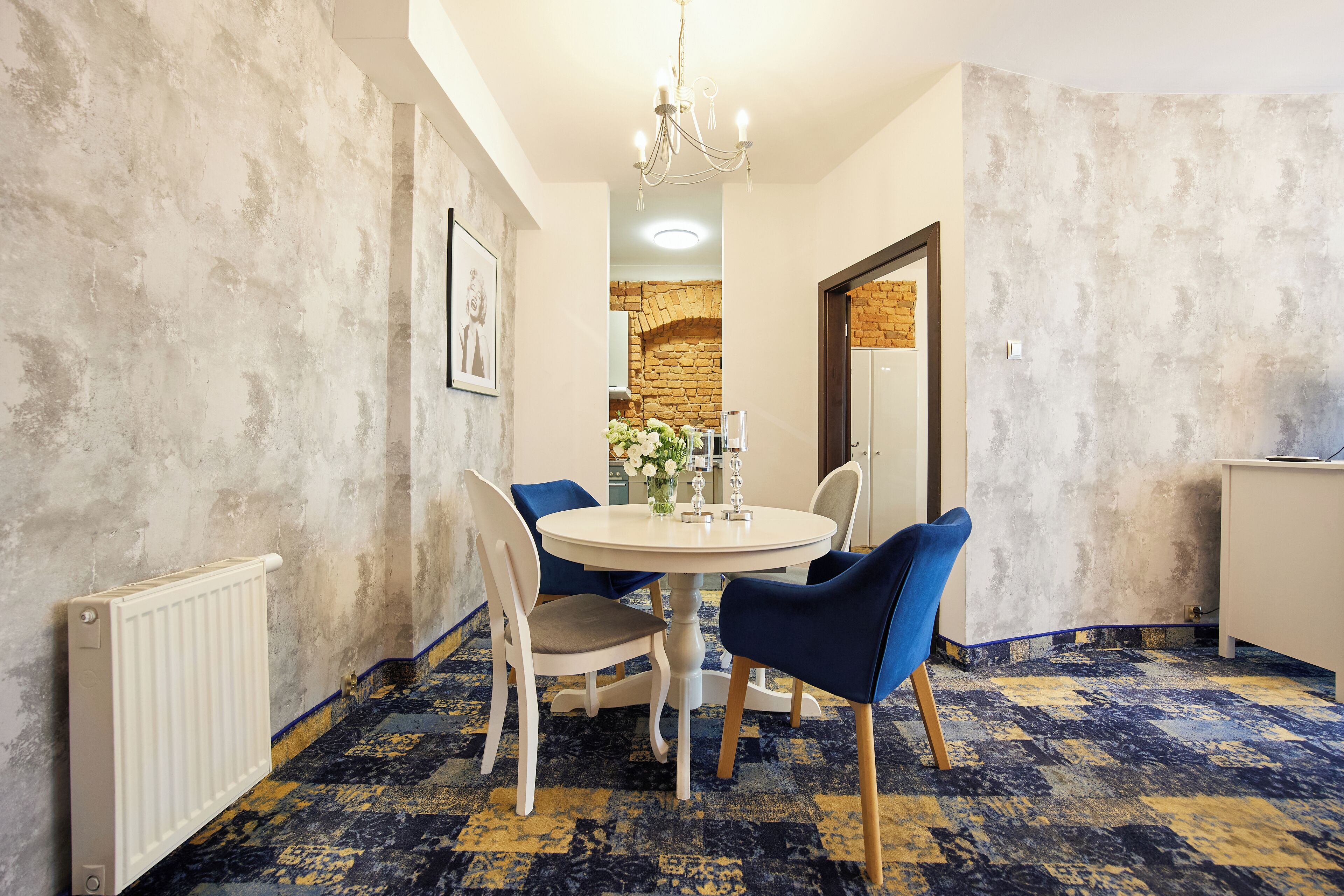 A dining area with a round table, blue chairs, a white radiator, and a patterned carpet.