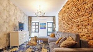 A living room with a brick wall, a sofa, a coffee table, and a TV. - Apartamenty By Bogunia (Bielsko-Biala)