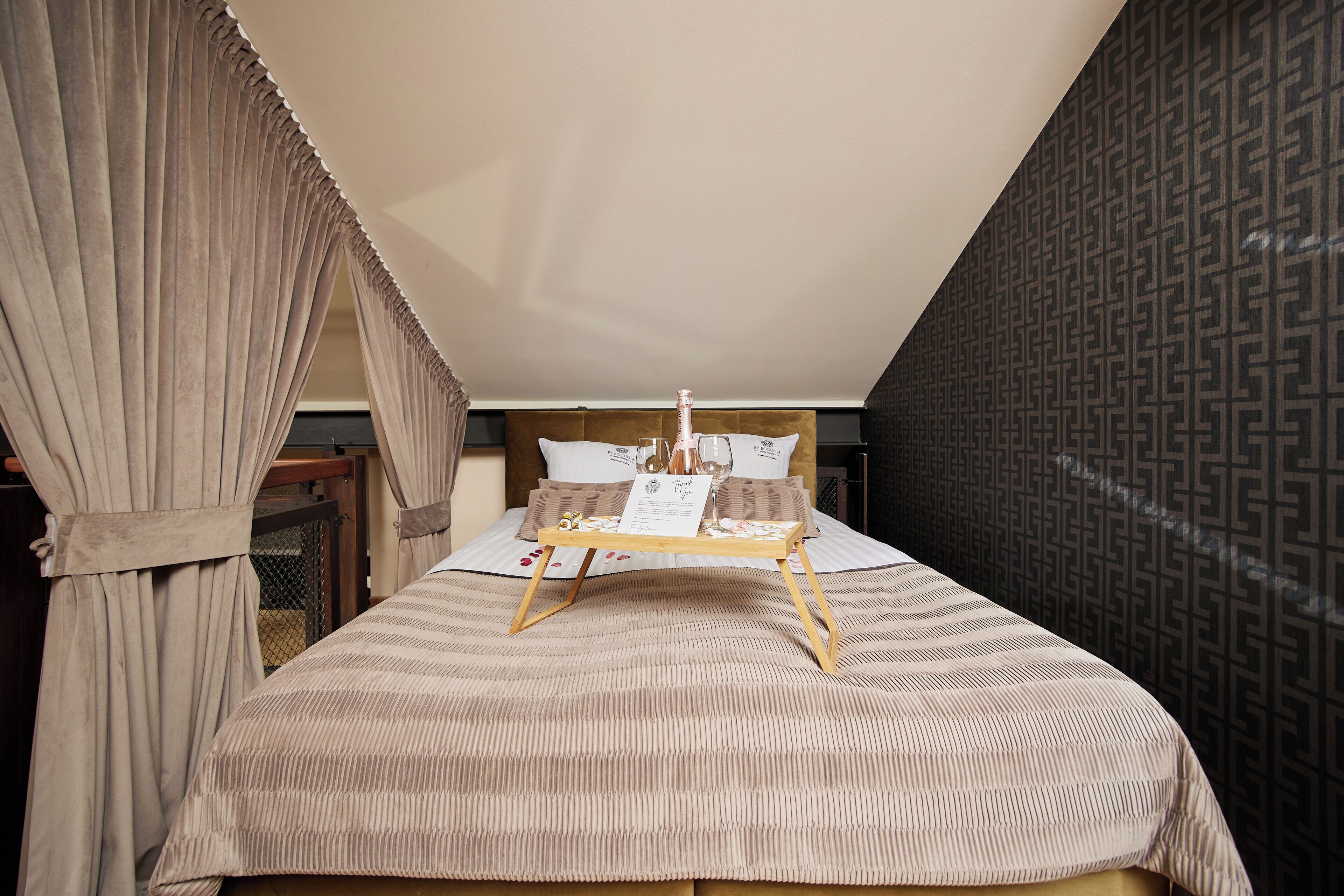 A bedroom with a bed, a tray with a bottle and glasses, and a patterned wall.