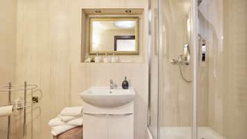 Un baño con un lavamanos blanco, un espejo con marco dorado, un box de ducha de cristal y un perchero para toallas.