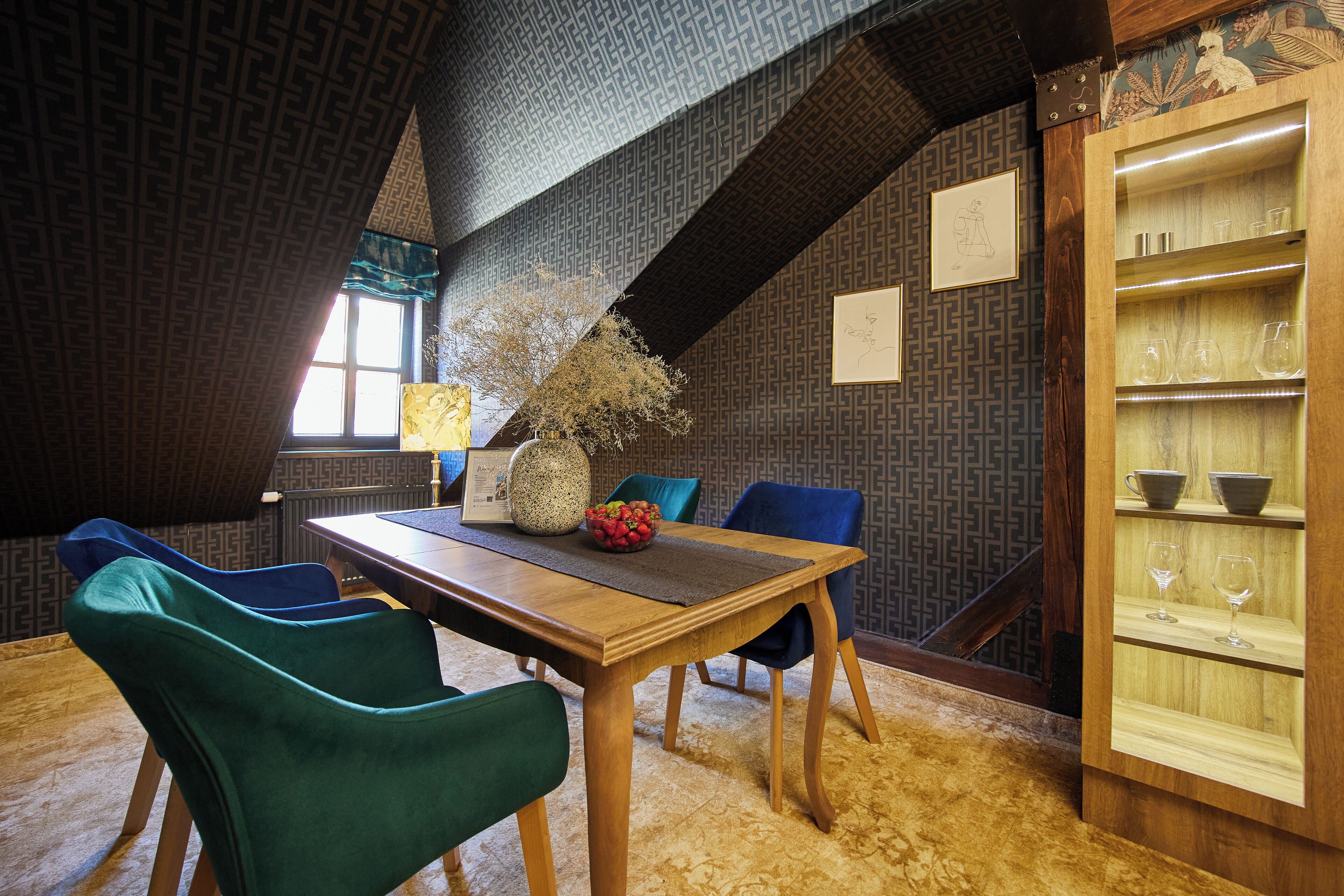 A dining area with a wooden table, teal chairs, and a patterned wall.