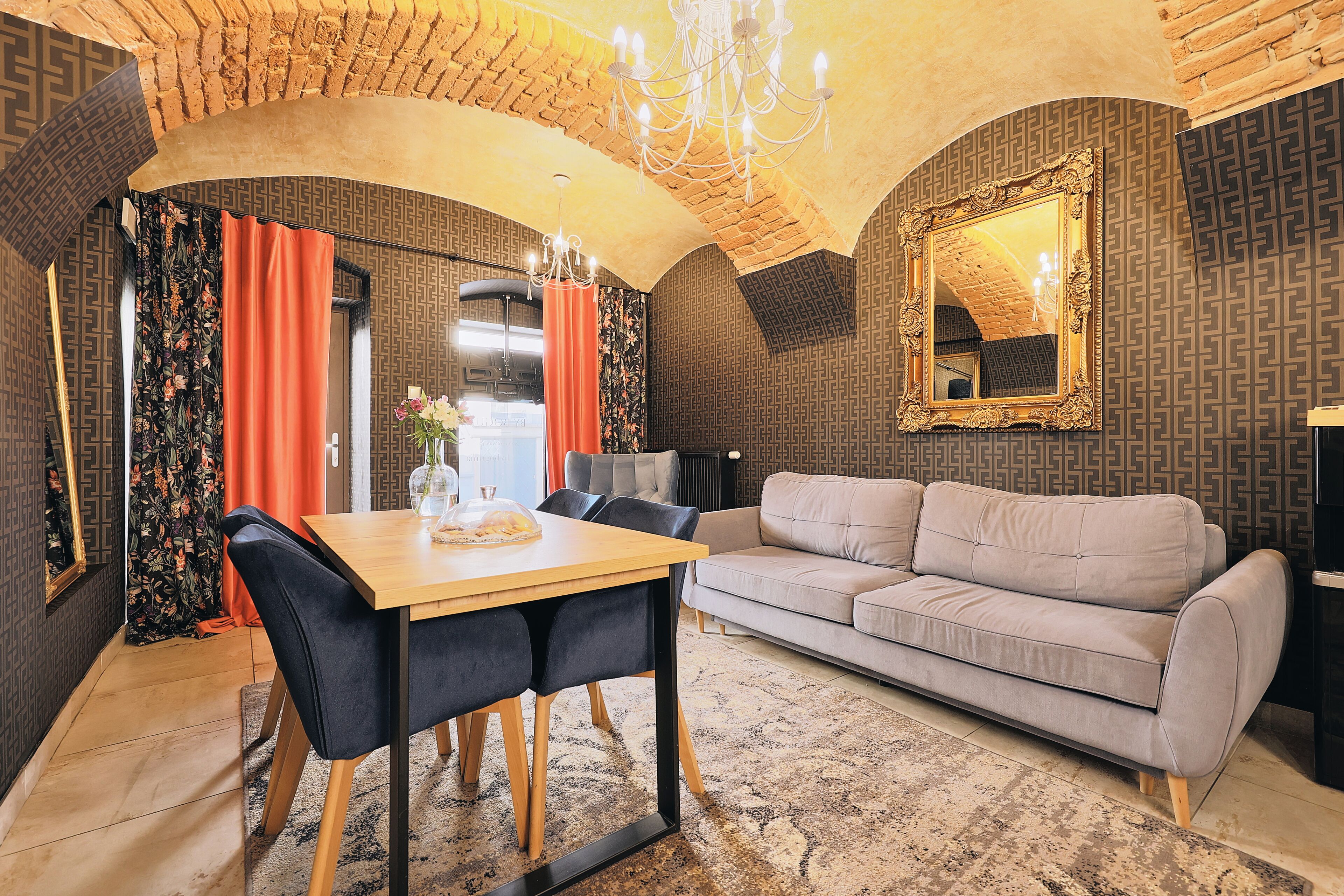 Un soggiorno moderno con un tavolo da pranzo in legno, sedie scure, un divano grigio e un tappeto decorato.
