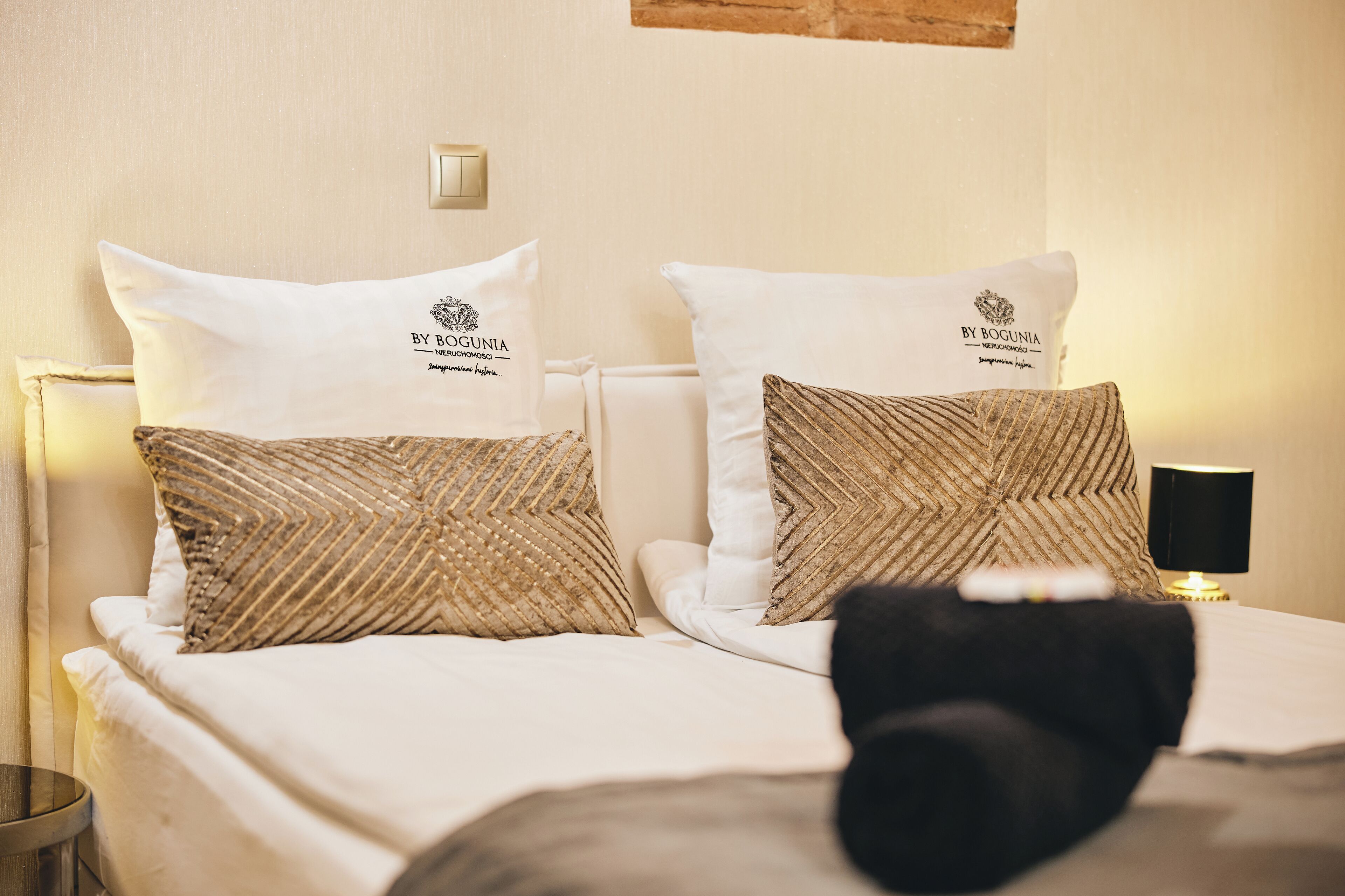 Ein Hotelzimmer mit zwei Betten, jeweils mit einem weißen und einem gemusterten Kopfkissen, einem Nachttisch mit Lampe sowie einem an der Wand befestigten Lichtschalter.