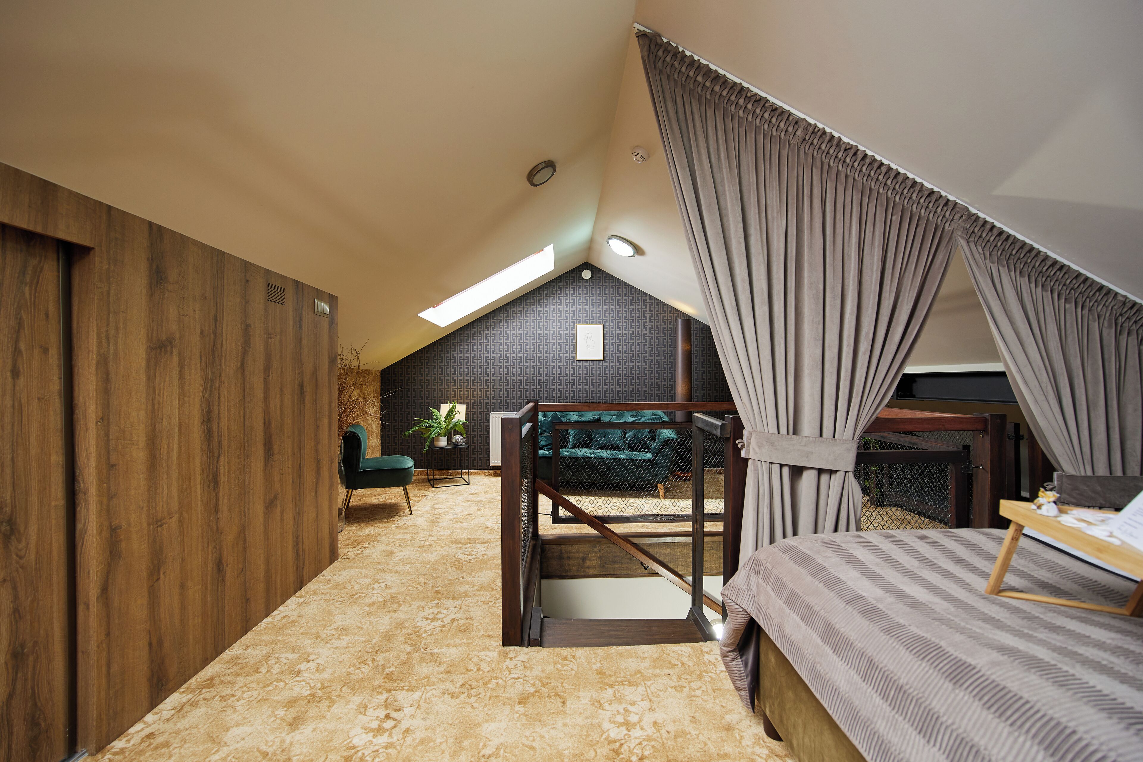 Quarto com teto inclinado, cama, escrivaninha e vista para o exterior.