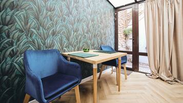 A room with a wooden herringbone floor, a table with a green placemat, two blue chairs, and a patterned wallpaper.