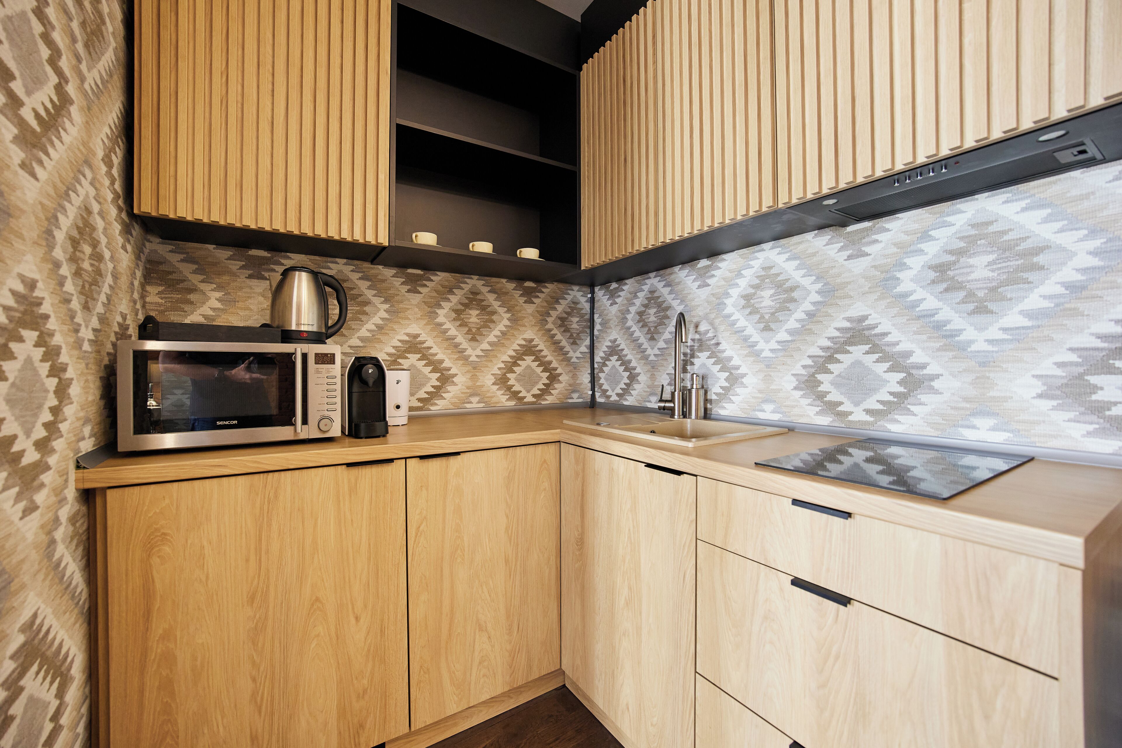 A kitchen with wooden cabinets, a microwave, a kettle, and a sink.