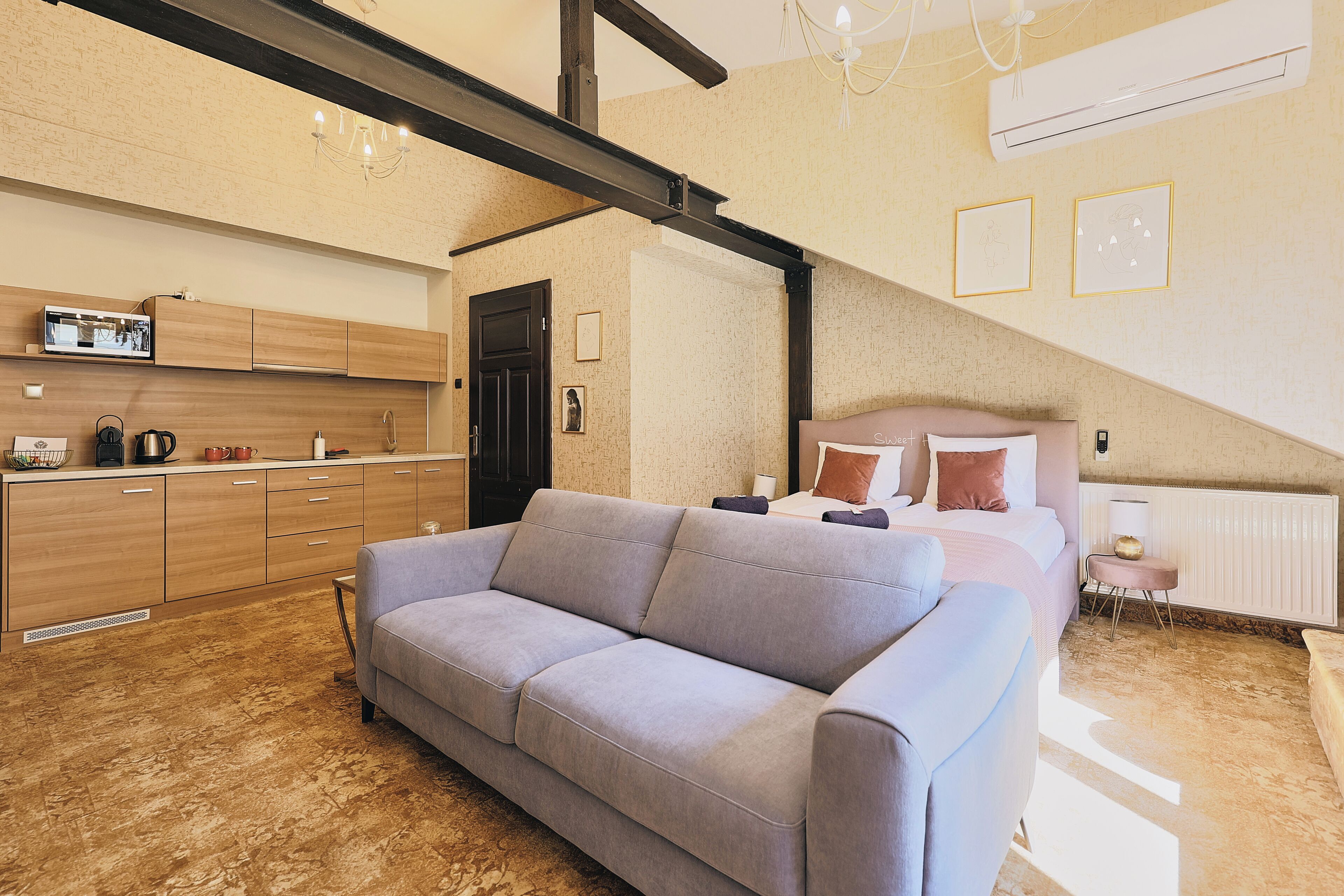 A modern, well-lit room with a sofa, a bed, and a kitchenette.