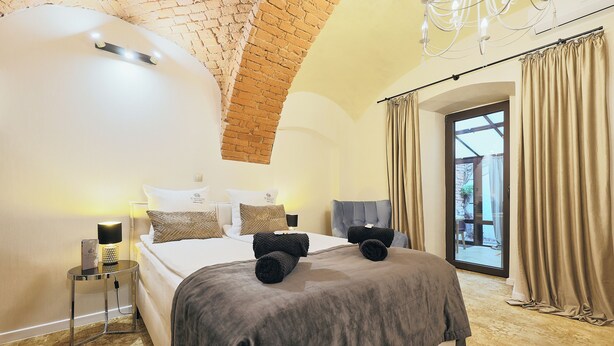 A bedroom with a bed, a nightstand, a lamp, and a view of the outside. - Apartamenty By Bogunia (Bielsko-Biala)