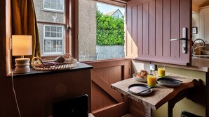 A cozy kitchen with a window, a lamp, a basket, a bowl of croissants, and a glass of orange juice. - Penn an Vownder (The Lizard)