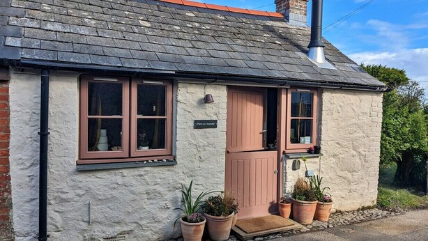 A quaint stone cottage with a red door, two windows, and a chimney. - Penn an Vownder (The Lizard)