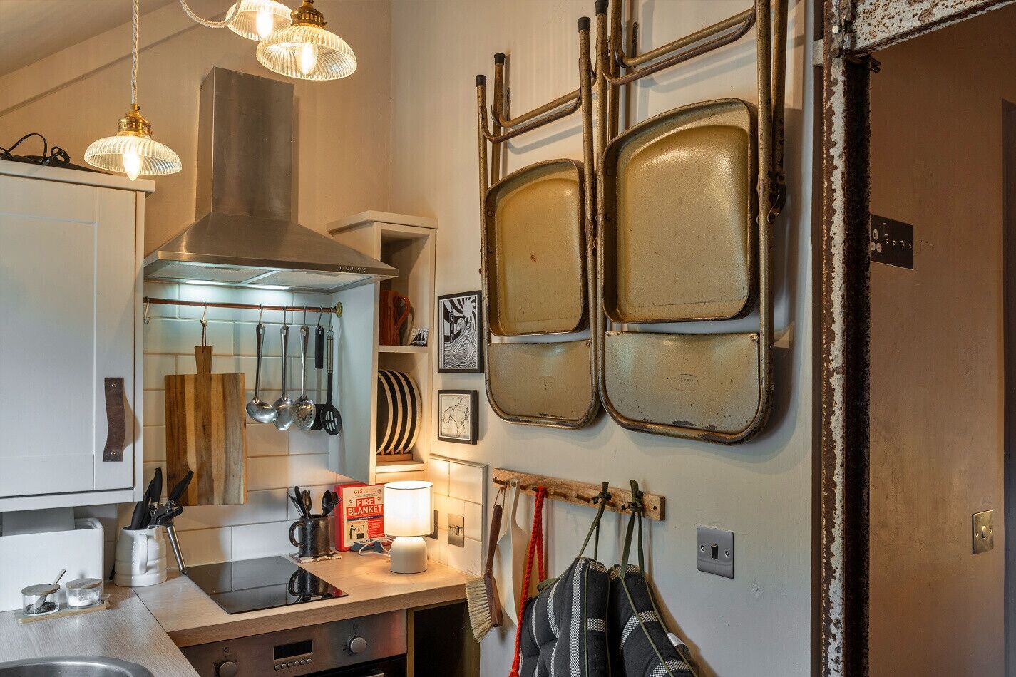A kitchen with a modern stove, hanging utensils, and a unique wall-mounted metal shelf.