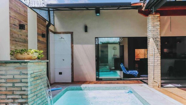 A pool area with a glass door leading to a room, a chair, and a stone wall.