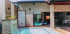 Zona de piscina con puerta de cristal que da a una habitación, una silla y un muro de piedra.