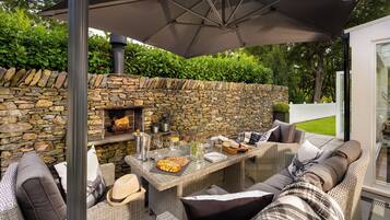 Un patio al aire libre con mobiliario de mimbre, un muro de piedra y una chimenea.