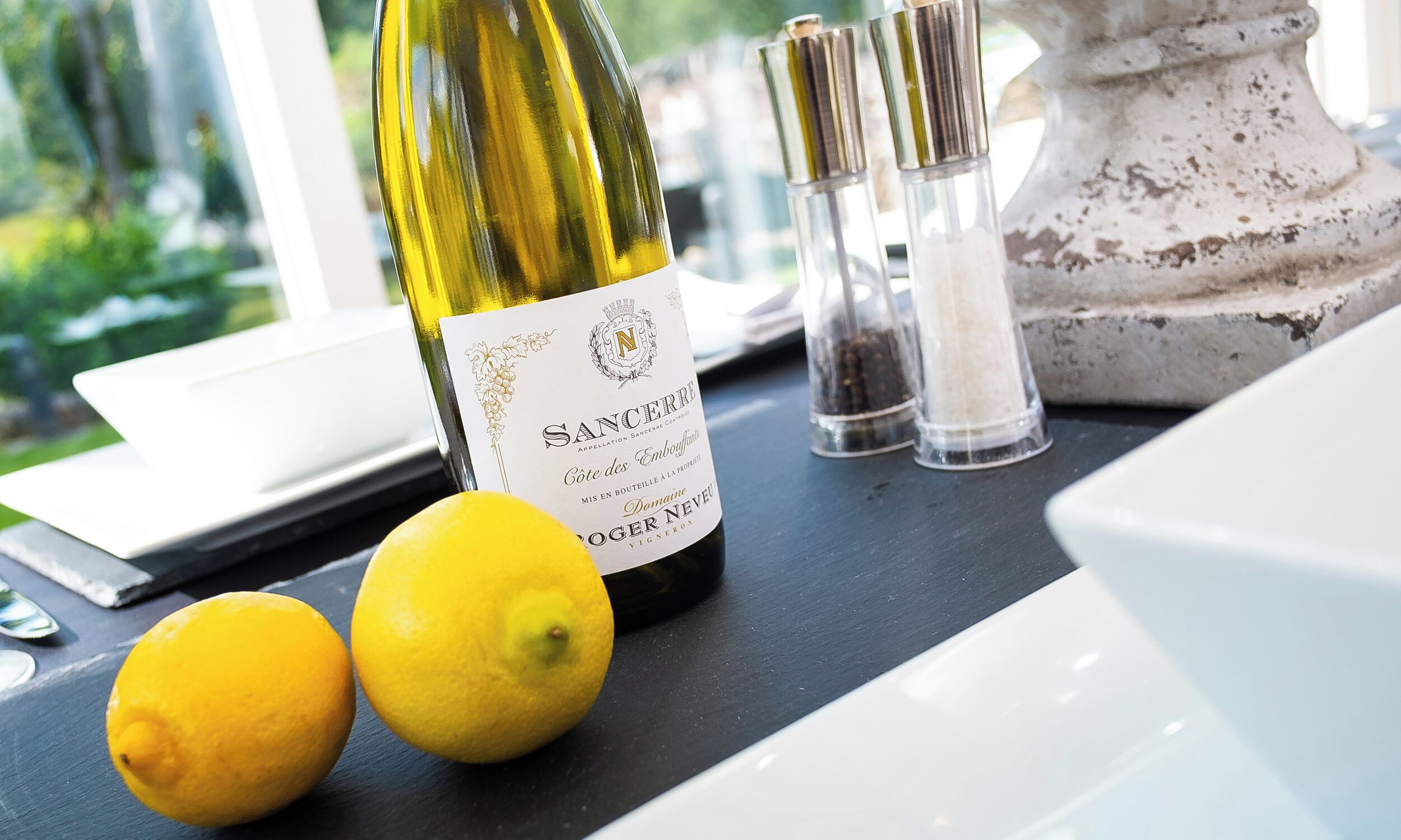 A bottle of Sancerre wine, two lemons, and salt shakers on a table.