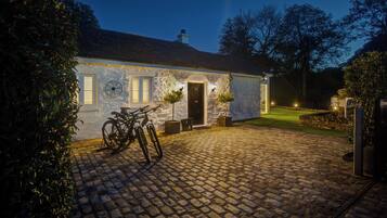 Un edificio de piedra con un camino de adoquines, una bicicleta y una entrada bien iluminada.