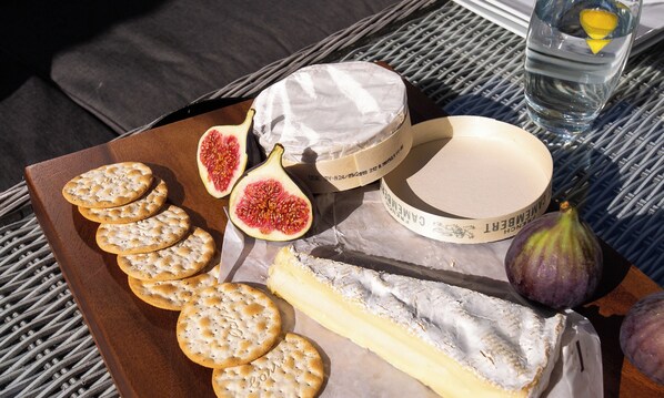 A cheese board with crackers, a halved fig, a wheel of cheese, a small bowl, and a glass of water on a table. - River Barn (Grange-over-Sands)