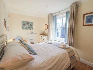 A bedroom with a large bed, a dresser, a nightstand, a window with curtains, and a painting on the wall. - Two Tweenways (Ambleside)