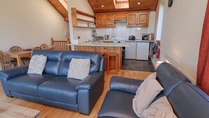 Una sala de estar acogedora con un sofá de cuero azul y un otoman a juego, una mesa de comedor de madera y una cocina con armarios de madera y una pequeña isla.