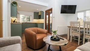 A modern living room with a brown leather sofa, a round wooden coffee table, and a dining area with a wooden table and chairs. - Esk Pike (Windermere)