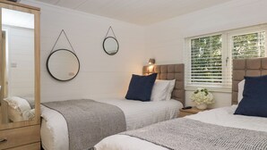 A bedroom with two beds, a wooden wardrobe, a mirror, and a window with blinds. - Esk Pike (Windermere)