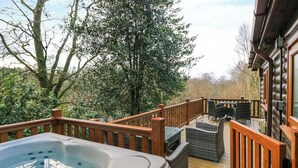 A wooden deck with a hot tub, wicker furniture, and a view of trees and a building. - Esk Pike (Windermere)