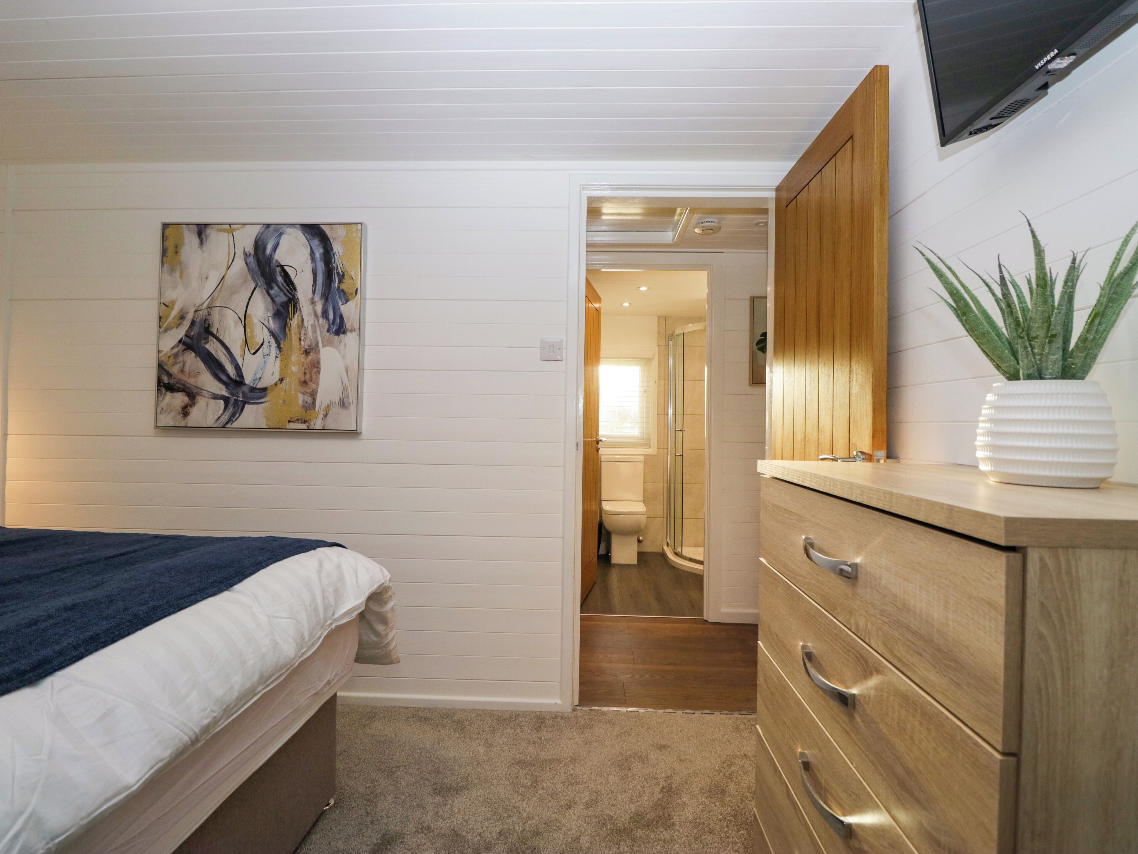 A bedroom with a bed, a dresser, a TV, and a painting on the wall.
