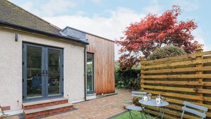 A patio with a table and chairs, a wooden fence, and a house with a sliding glass door. - Esk Brae (Langholm)