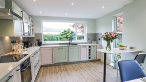 A modern kitchen with light-colored cabinets, a large window, and a dining area with a table and chairs. - Esk Brae (Langholm)