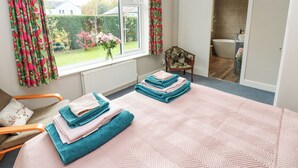 A bedroom with a large bed, a chair, a window with curtains, and a view of a garden. - Esk Brae (Langholm)