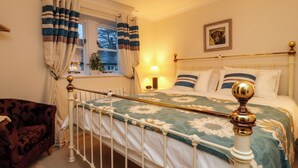 Een slaapkamer met een bed, een stoel, een raam met gordijnen, een lamp en een ingelijst schilderij aan de muur.