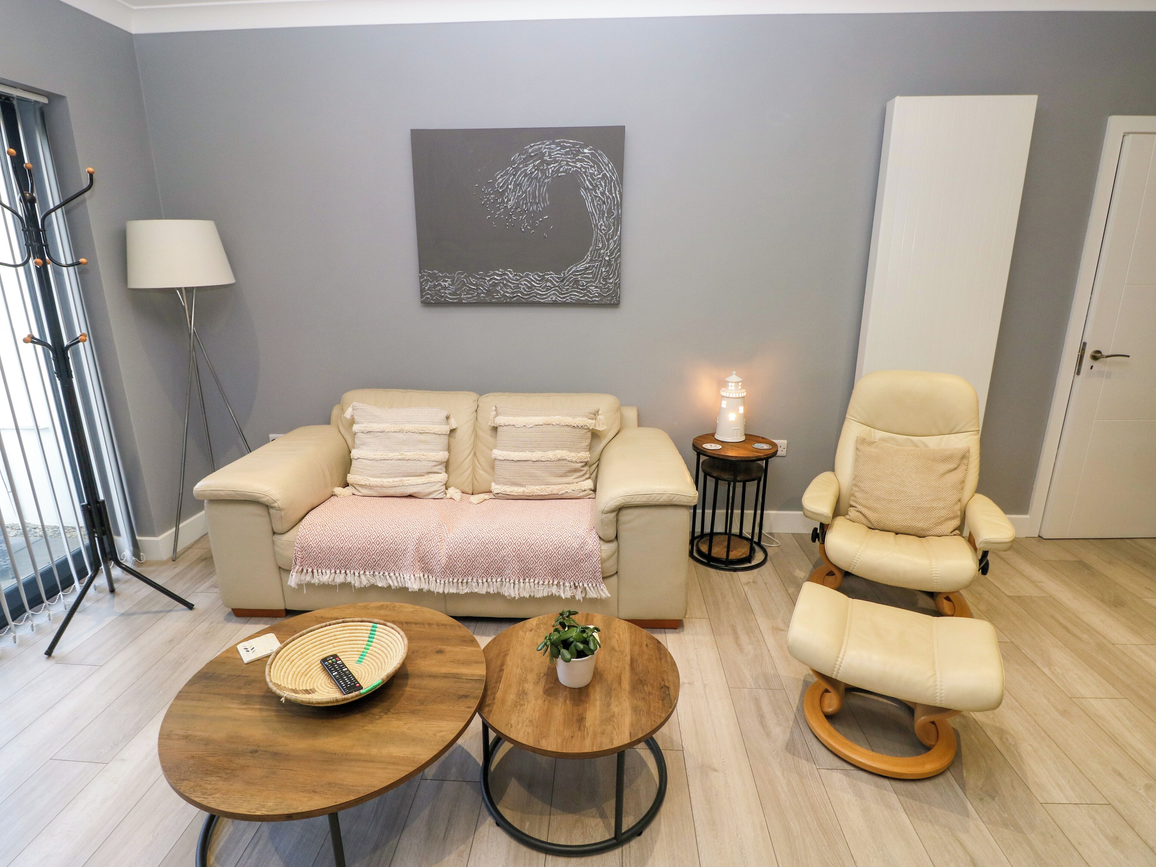 A modern living room with a sofa, armchair, coffee table, and a small table with a lamp.
