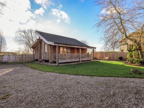 A wooden cabin with a porch, surrounded by a gravel driveway and a grassy yard. - Cedrus Lodge (Penrith)