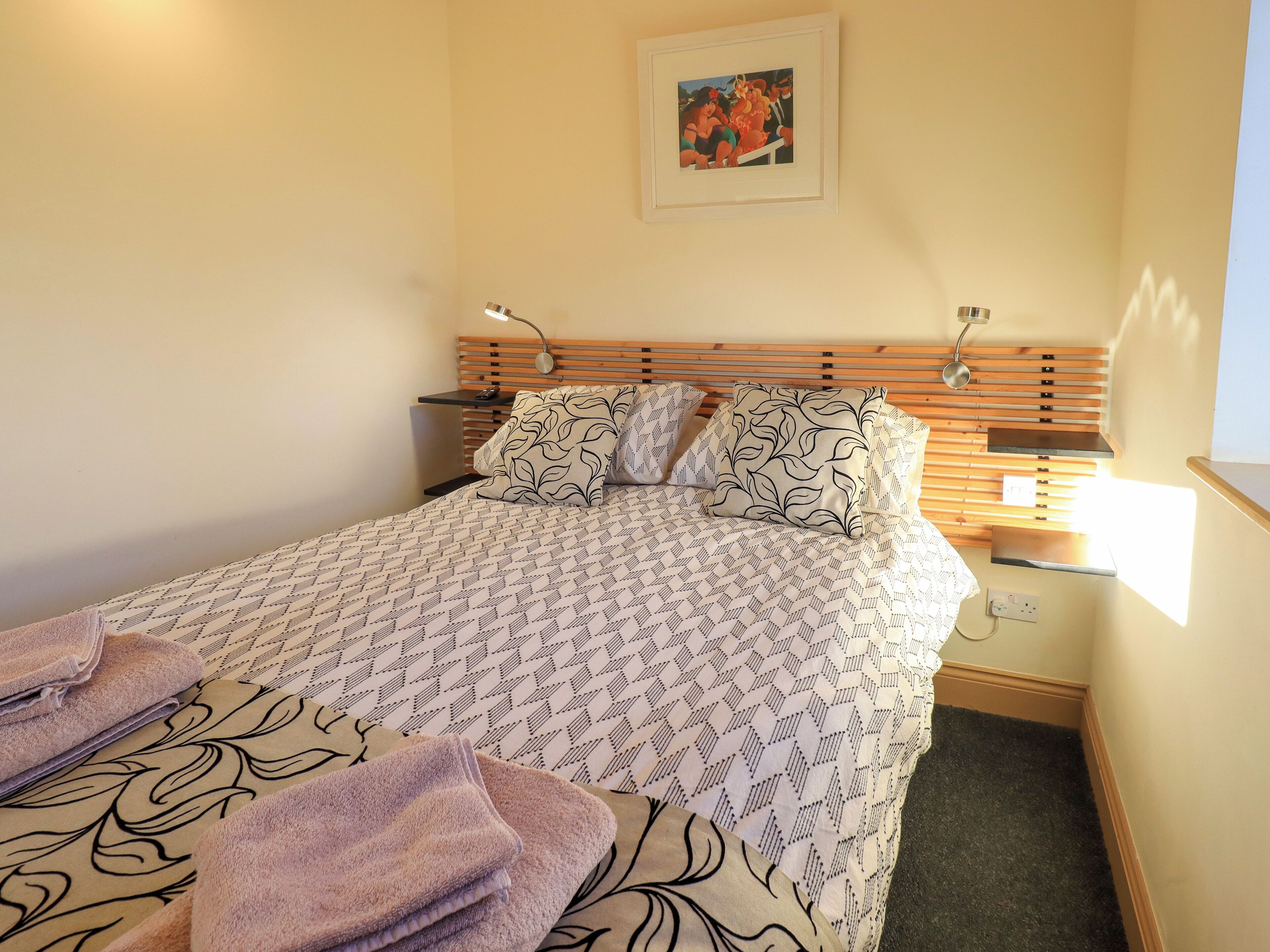 A neatly made bed with patterned bedding and pillows, a bedside table with a lamp, and a framed picture on the wall.