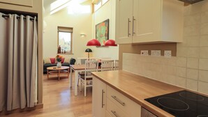 Une cuisine moderne avec des plans de travail en bois, une plaque de cuisson à induction noire et des armoires blanches. On y trouve un coin repas avec une table et des chaises, ainsi qu’une fenêtre qui laisse entrer la lumière naturelle.