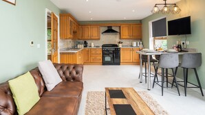 A modern kitchen with wooden cabinets, a black stove, and a dining area with bar stools. - Carreg Wen (Harlech)
