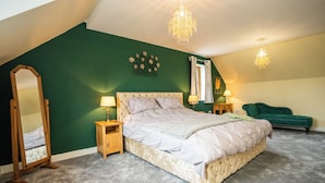 A bedroom with a large bed, two bedside tables, a mirror, a chandelier, and a green upholstered chair. - Carreg Wen (Harlech)