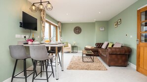 A modern living room with a brown leather sofa, a dining area with a table and chairs, and a TV mounted on the wall. - Carreg Wen (Harlech)