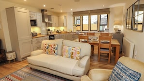 A compact living space with a kitchenette, a dining area, and a sofa with patterned cushions. - Deer Wood At Applethwaite Hall (Windermere)